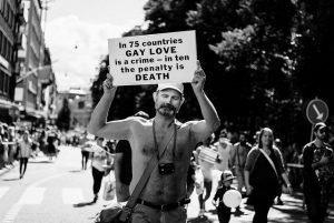 A man holds a signs that says "In 75 countries Gay Love is a crime - in ten the penalty is death."