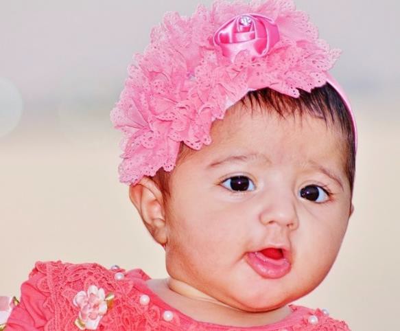 A female infant wearing stereotypically feminine clothing and accessories.