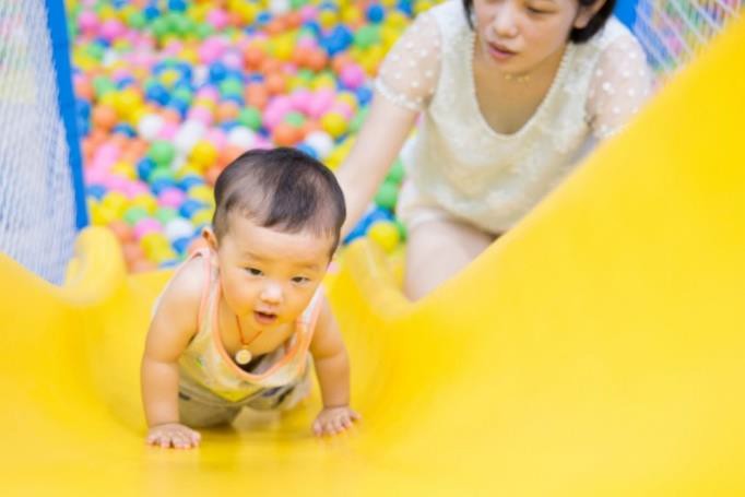 A mother offering a secure base as her infant plays on a slide.