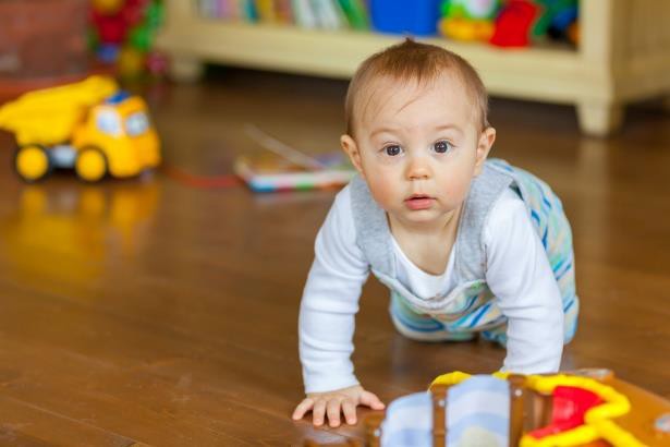 An infant crawling on the floor with toys around as done in the Strange Situation.