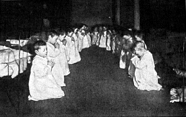 This is a residential nursery in 1888. Young children are praying on their knees in their bedclothes.