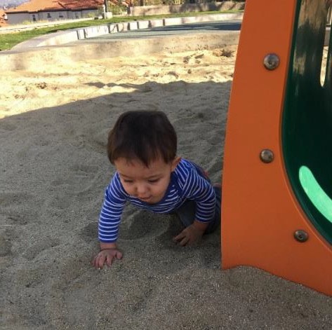 An infant playing in the sand.