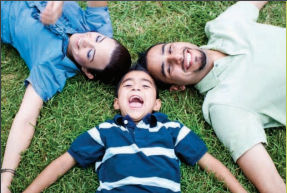 Two adults and a child laugh together while laying on the grass.