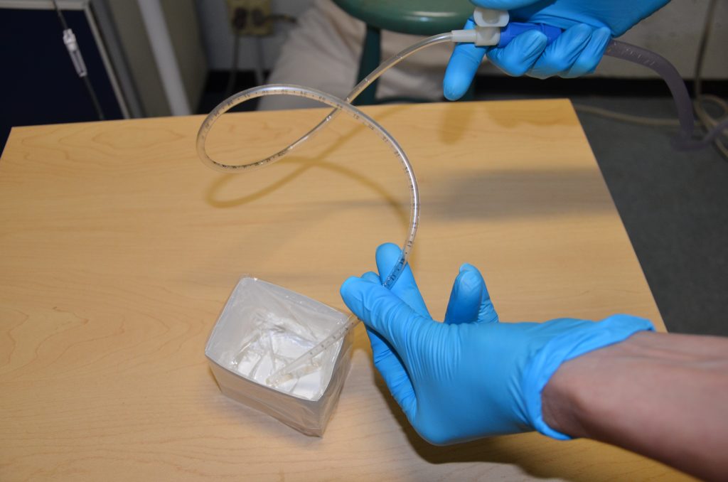 Photo of a sterile suction catheter being handled by a person wearing gloves