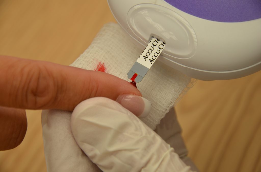 Photo showing the obtainment of a drop of blood on a medical strip