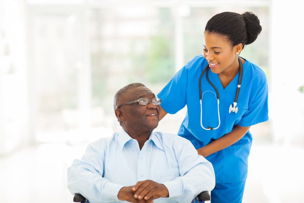 Image of a female health care professional smiling down at a patient sitting in a wheelchair.