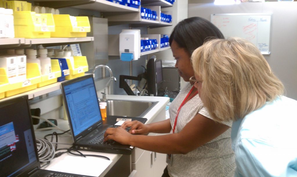 Image showing two nurses in a pharmacy, entering information into electronic health record on a laptop