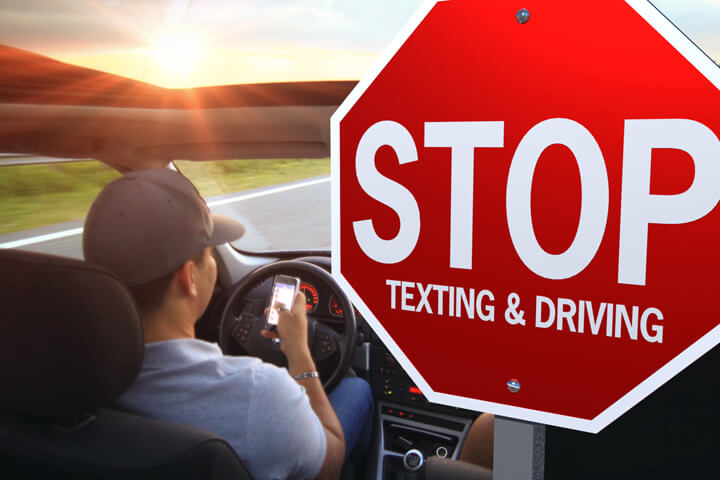 Photo showing car driver looking at cell phone with large stop texting and driving sign beside them