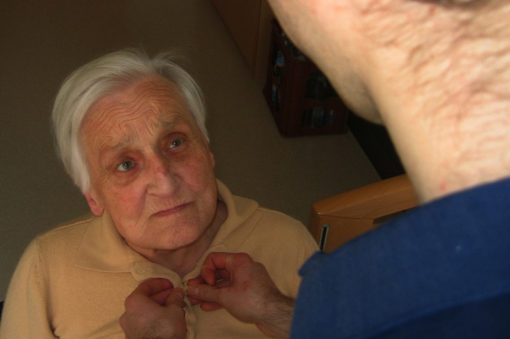Image of a dementia patient receiving assistance with buttoning a shirt