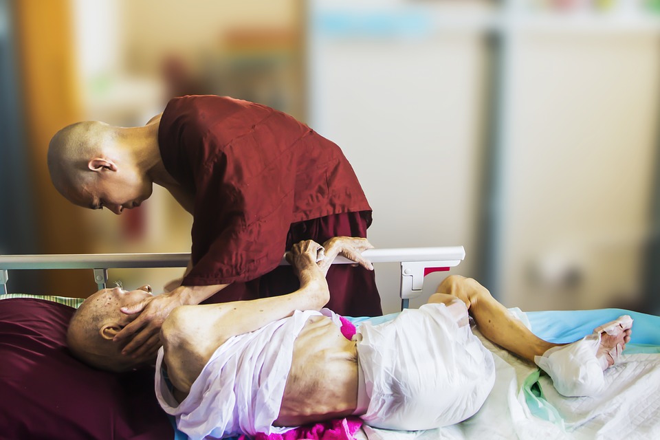 Image showing a monk leaning over a hospice patient and touching their face