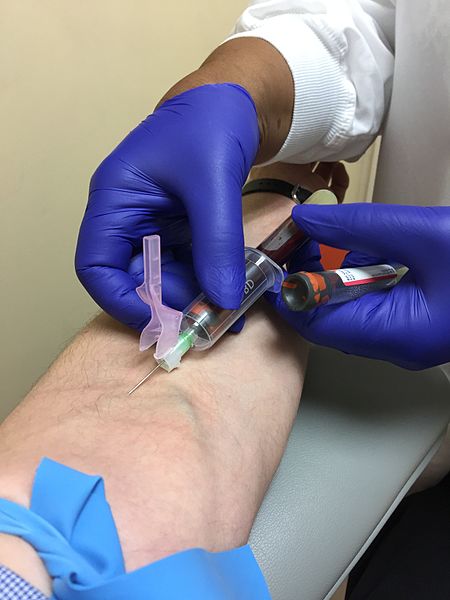 Photo showing gloved medical professional hands performing a Venipuncture