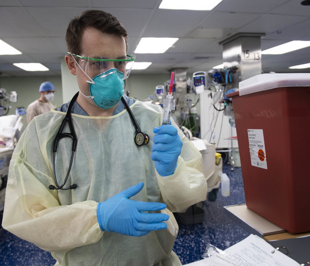Photo showing a navy medical personal wearing an isolation gown and other P P E