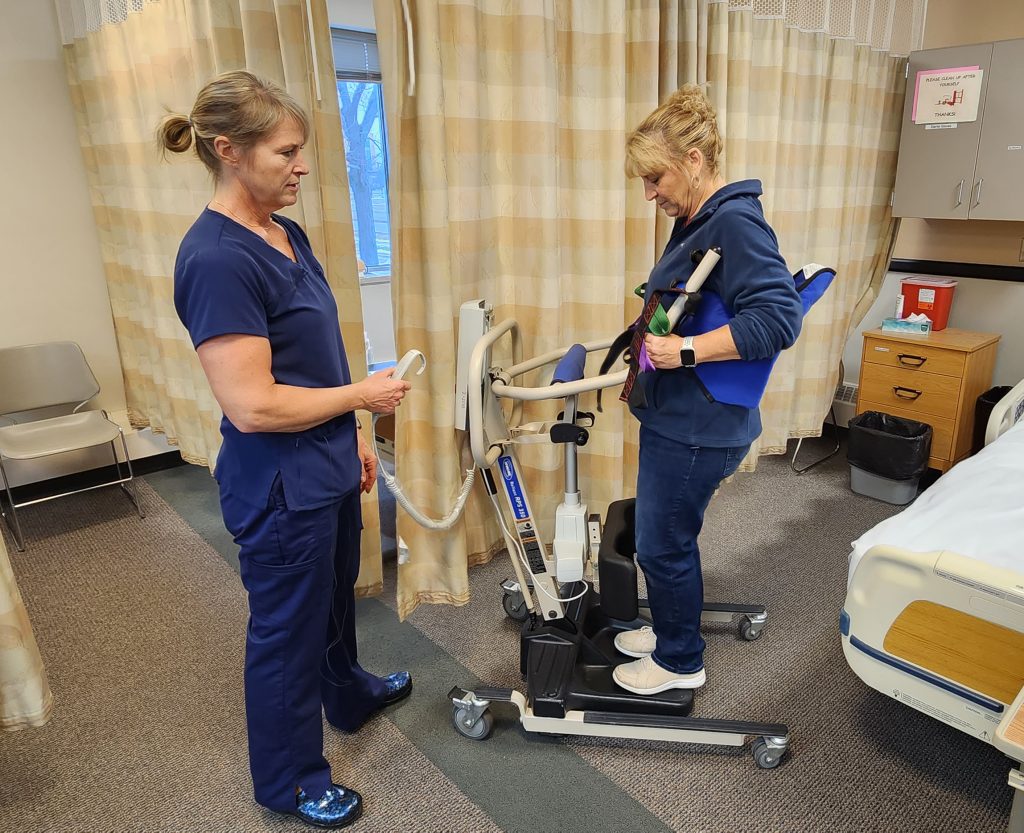 Photo showing a nurse using a sit-to-stand lift with a simulated patient.