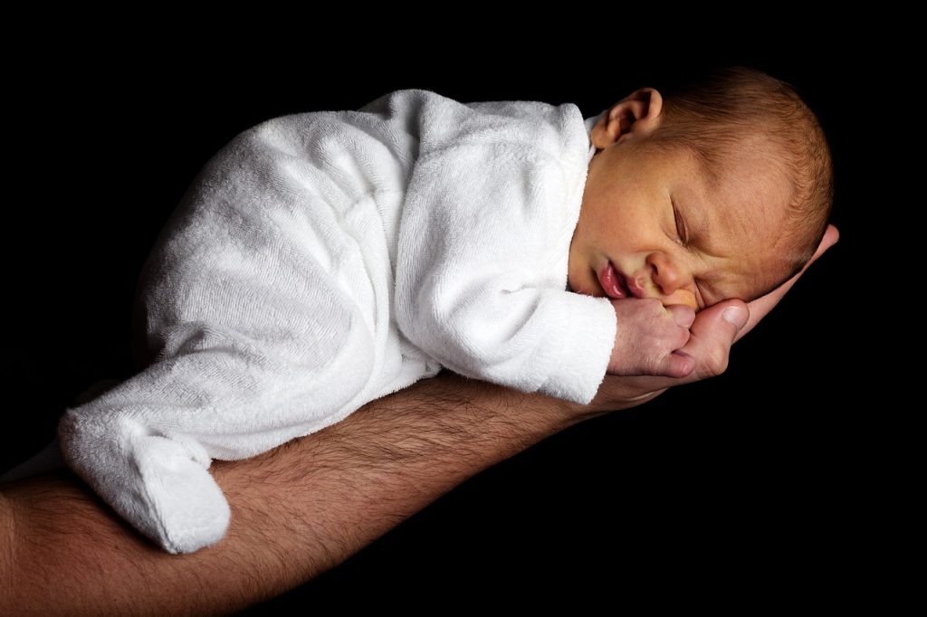 Photo showing a newborn laying on its stomach across someone's hand and forearm