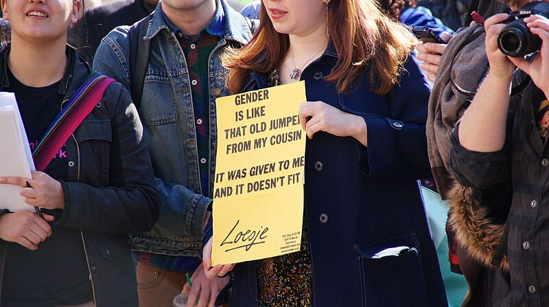 An unidentified person holds a sign that reads, "Gender is like that old jumper from my cousin: It was given to me and it doesn't fit," at a rally for transgender rights.