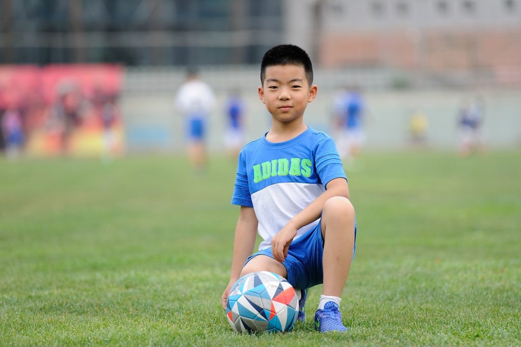 Photo showing a child kneeling with a soccer ball while facing the viewer