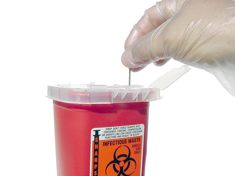 A gloved hand placing a needle into a sharps container