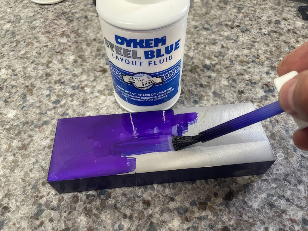 hand holding a brush is applying Layout fluid to a part surface