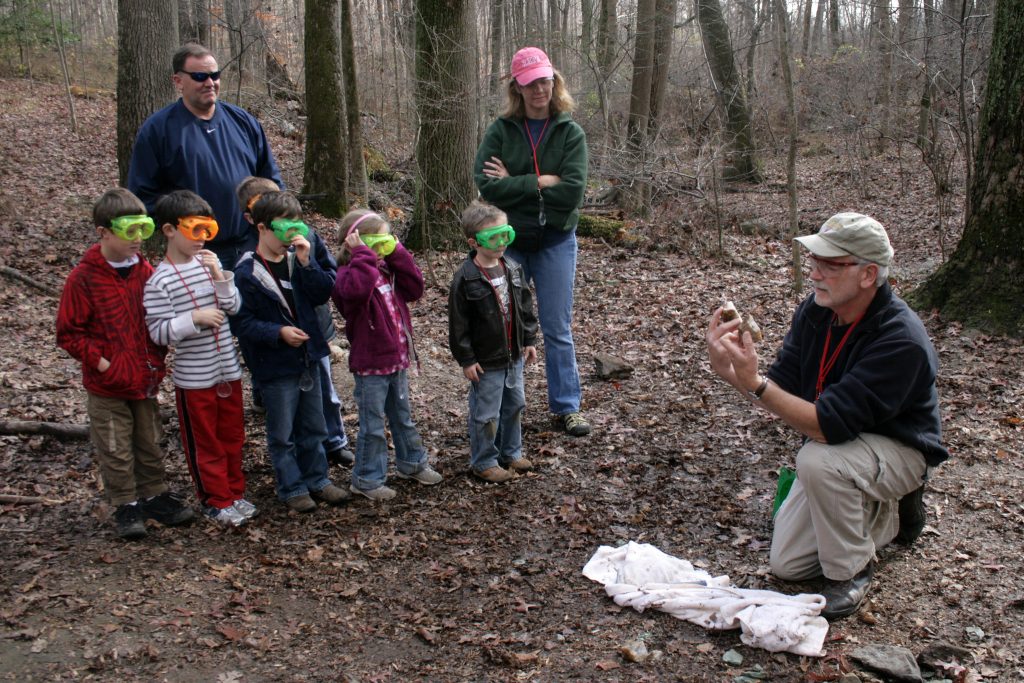 "4121373286_399f964496_k" by woodleywonderwork is licensed under CC BY 2.0 Several young children and three adults are outside in a wooded area. They appear to be learning about something related to the forest.