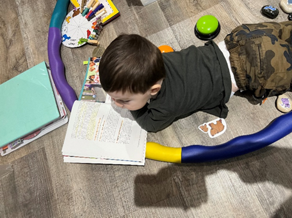 "untitled" by Mary Beth Boettcher is used with permission. Small child is laying on the floor, reading a book and surrounded by toys