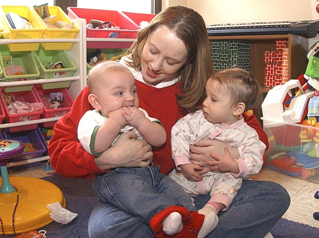"USMC-13222.jpg" by unknown author for U.S. Marines is in the Public Domain. The appearance of U.S. Department of Defense (DoD) visual information does not imply or constitute DoD endorsement. A caregiver is holding two older infants in her arms, while sitting on the floor in a care center.
