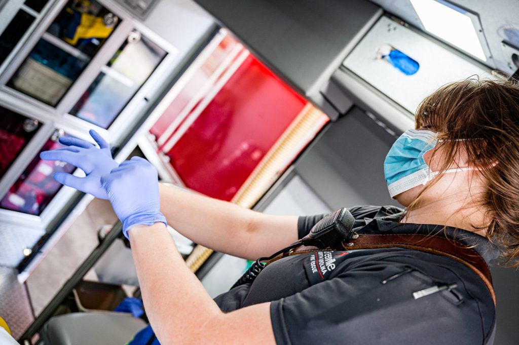 An E M R is donning gloves, while already wearing a mask