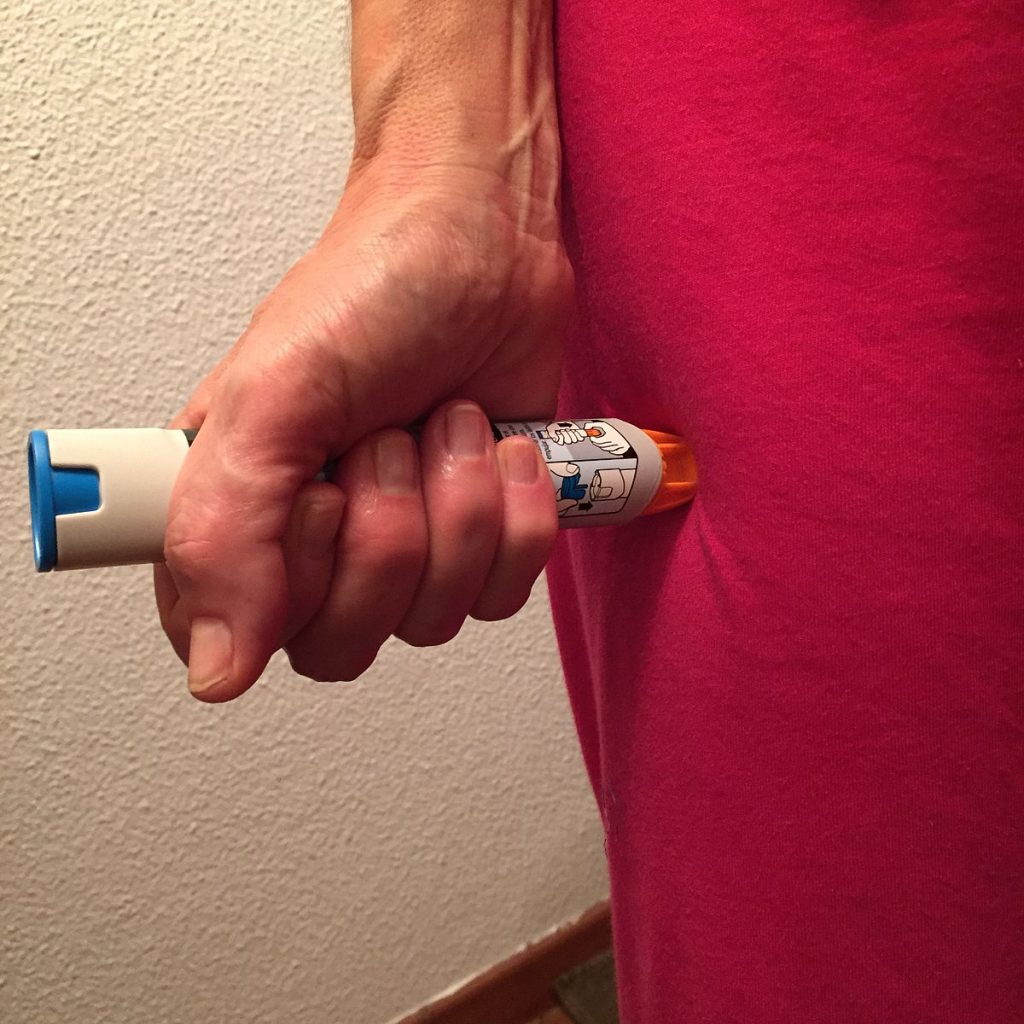 A test epi pen is being pressed against a persons upper leg