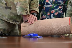 Military personnel are practicing the application of direct pressure to a simulated limb