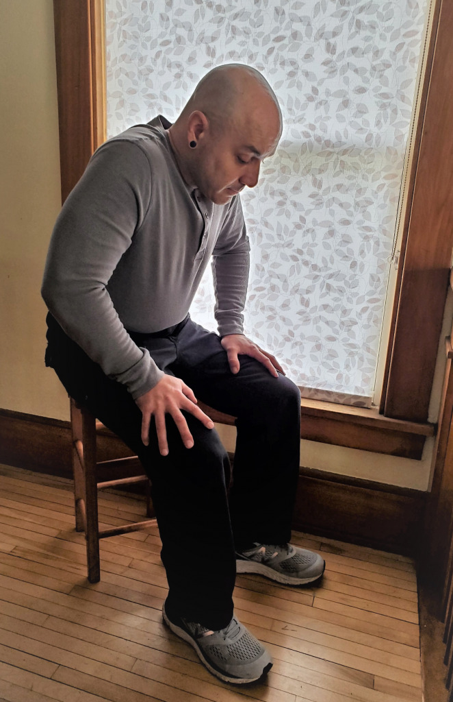 A person sitting in tripod position in front of a shaded window