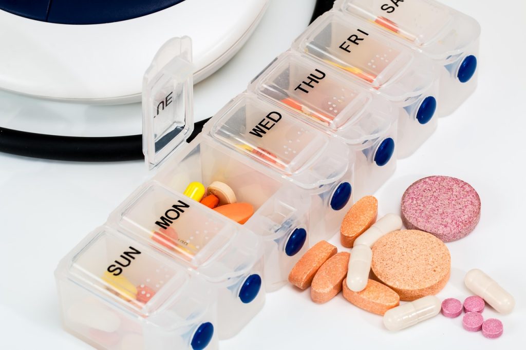 A weekly pill organizer with several pills resting outside of it