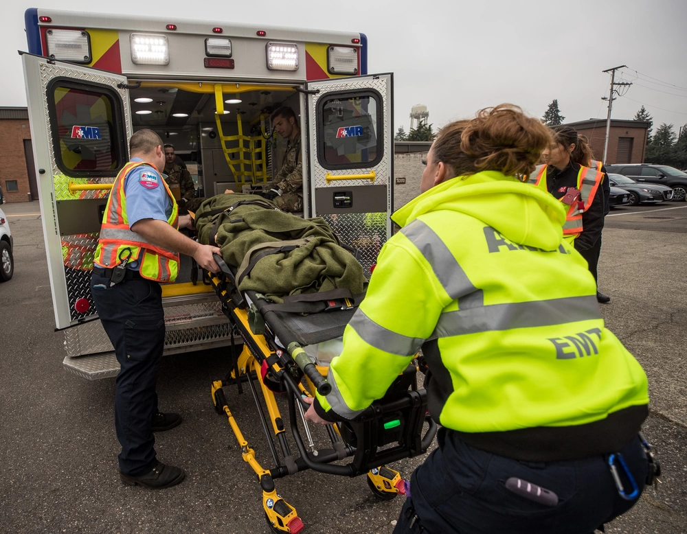 "Puget Sound Federal Coordinating Center National Disaster Medical System", by John Wayne Liston is in the Public Domain. The appearance of U.S. Department of Defense (DoD) visual information does not imply or constitute DoD endorsement. Emergency Responders are loading a patient on a stretcher into an ambuance