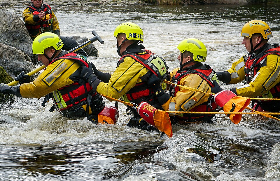 "Water_rescue_training" by Staffsfire is licensed under CC BY-SA 4.0 Five rescue workers are in rapidly moving water
