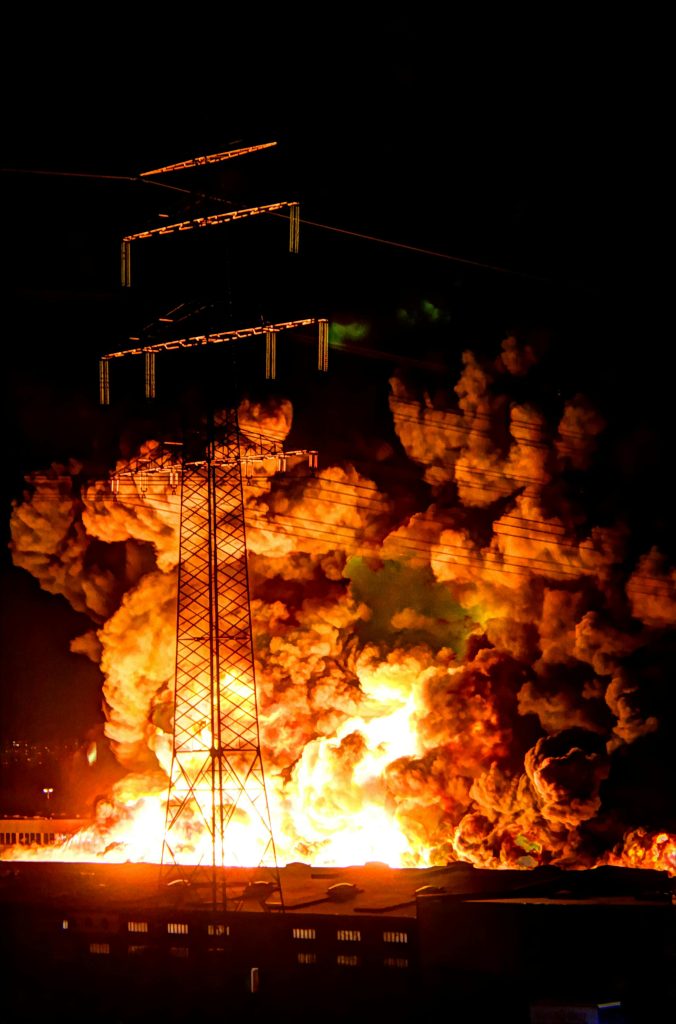 "pexels-torbenb-3623114" by Torben Bühl, via Pexels.com is licensed under CC0 A large, explosion and fire are seen behind a power line