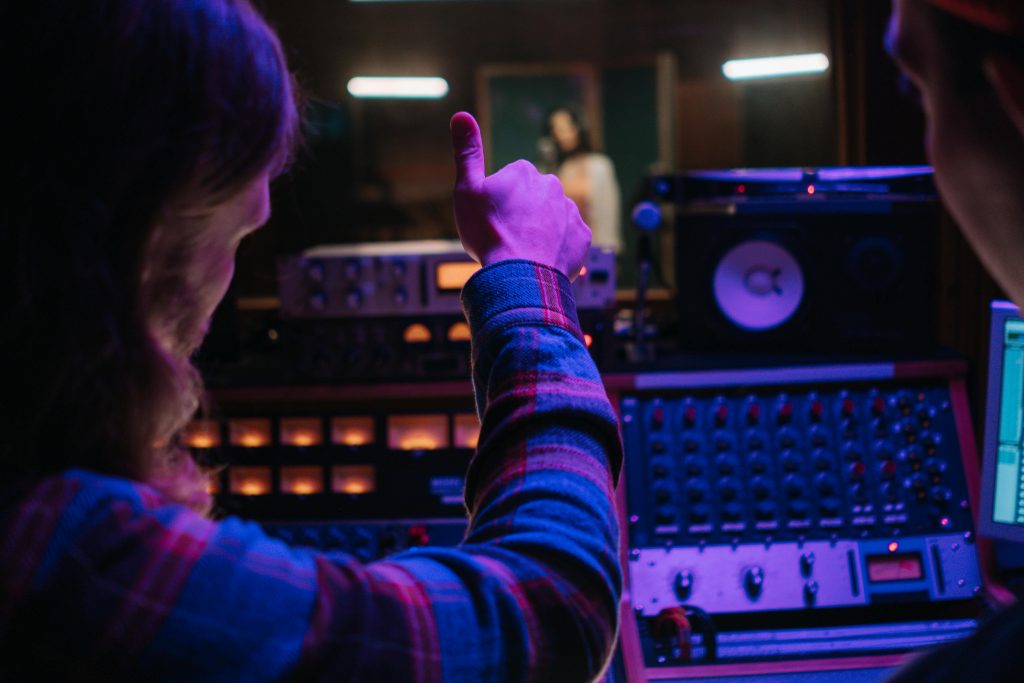 Person standing in front of audio mixing equipment, giving thumbs up to performer in background